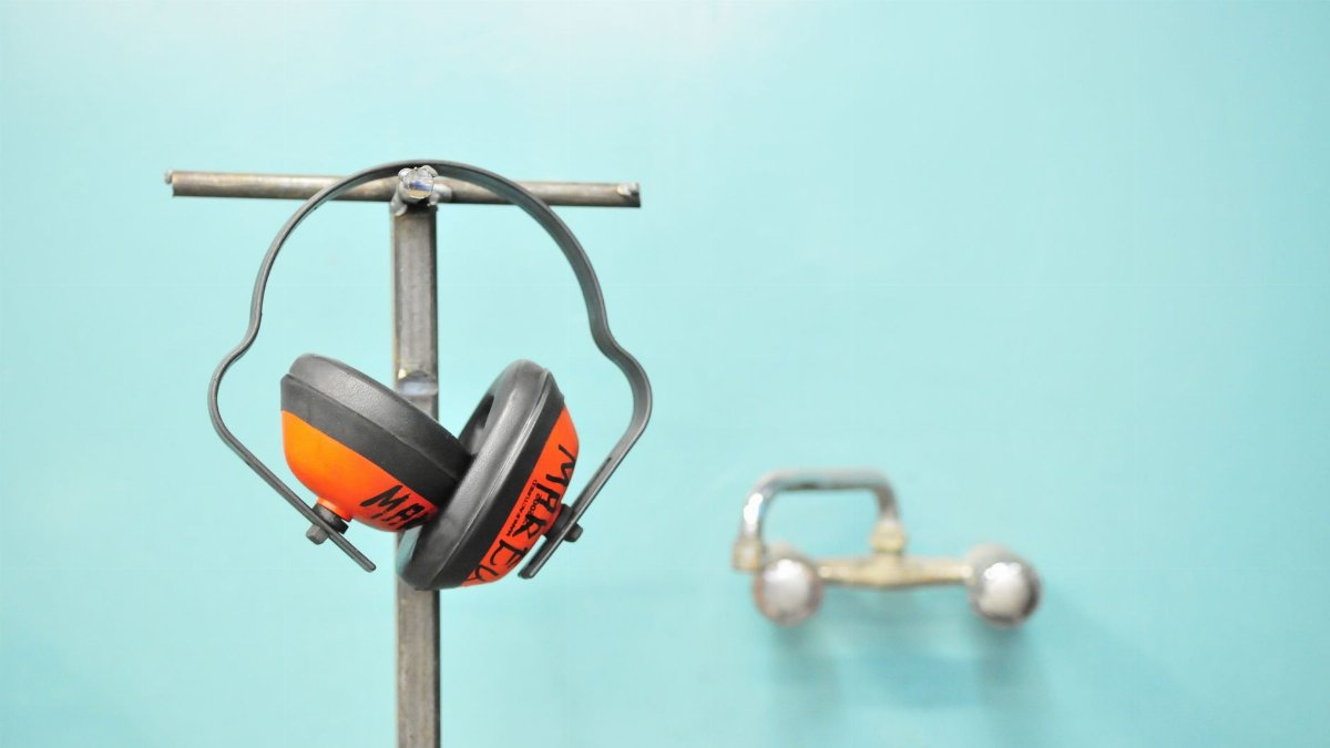Close-up of earmuffs hanging on a metal stand in front of a teal wall.