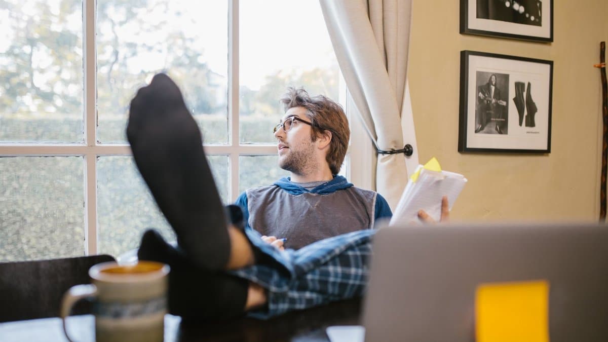 Man enjoying a relaxed home office setup with feet up, looking out the window.