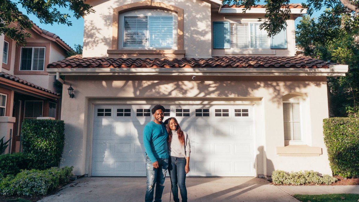 A joyous couple stands together in front of their newly purchased house, symbolizing new beginnings.