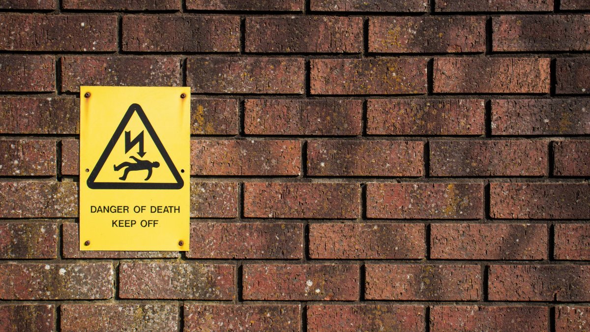 A bold warning sign on a brick wall displaying 'Danger of Death', emphasizing caution.