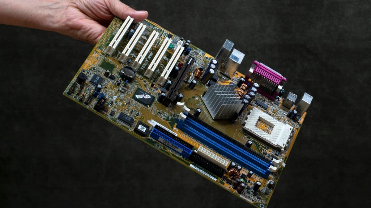 A close-up of a person's hand holding a computer motherboard against a dark background.