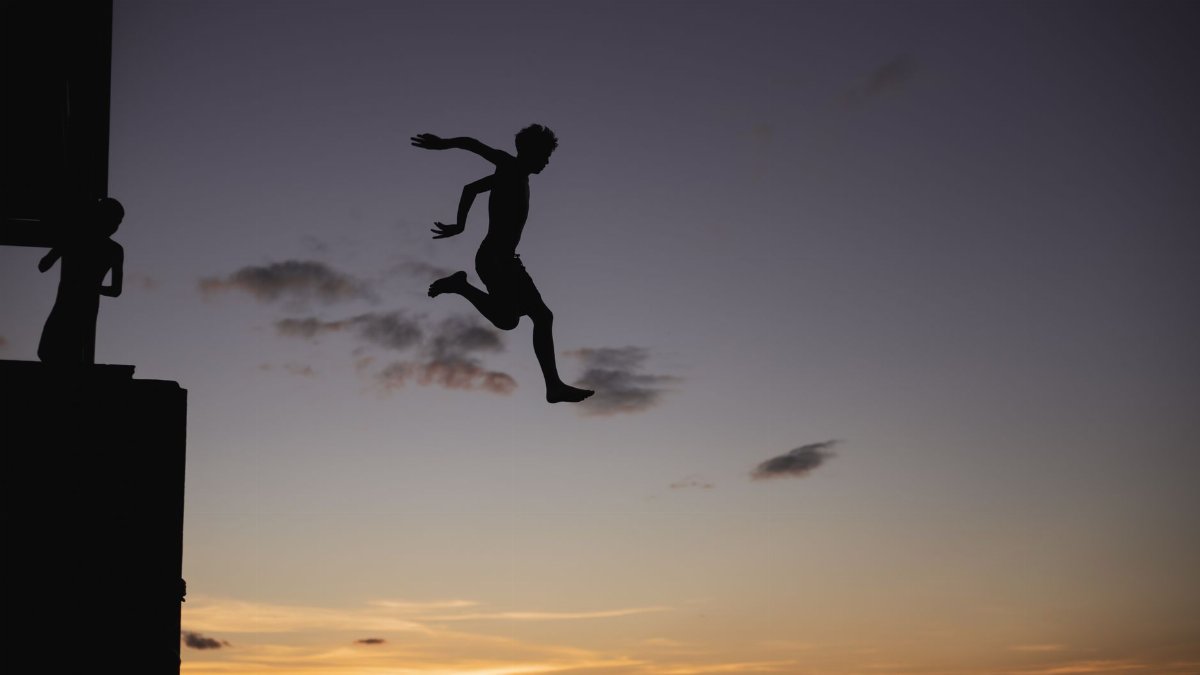Daring silhouette jump off a pier against a vibrant sunset sky, evoking adventure and bravery.