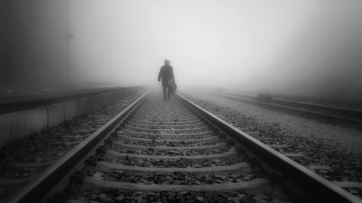 A man walks on foggy railroad tracks, conveying a sense of solitude and journey.