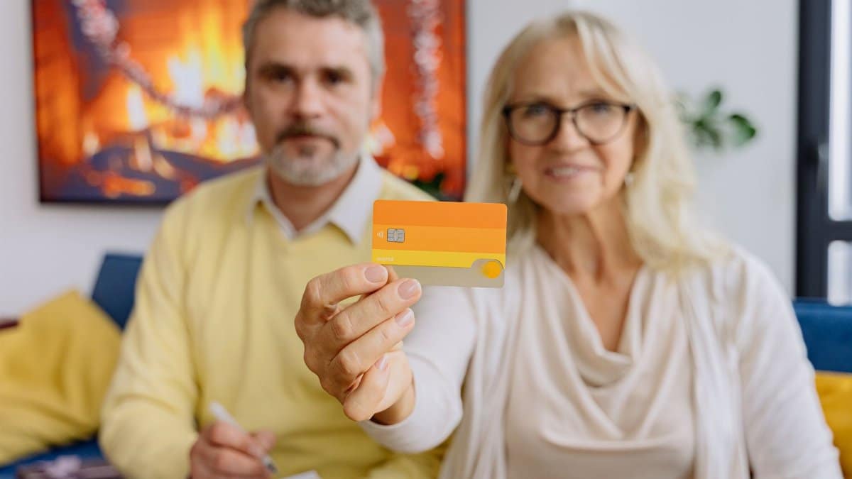 An elderly couple in a warm living room holding a credit card, symbolizing modern banking.