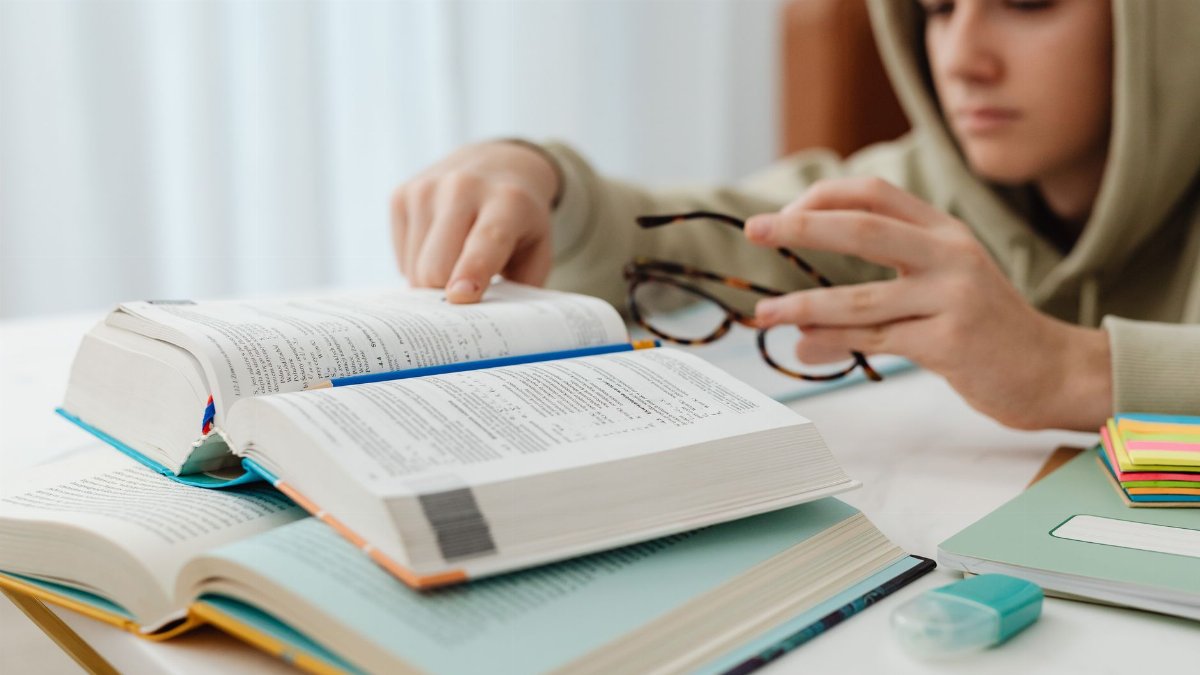Focused teenager studying with open textbooks, eyeglasses, and notes.