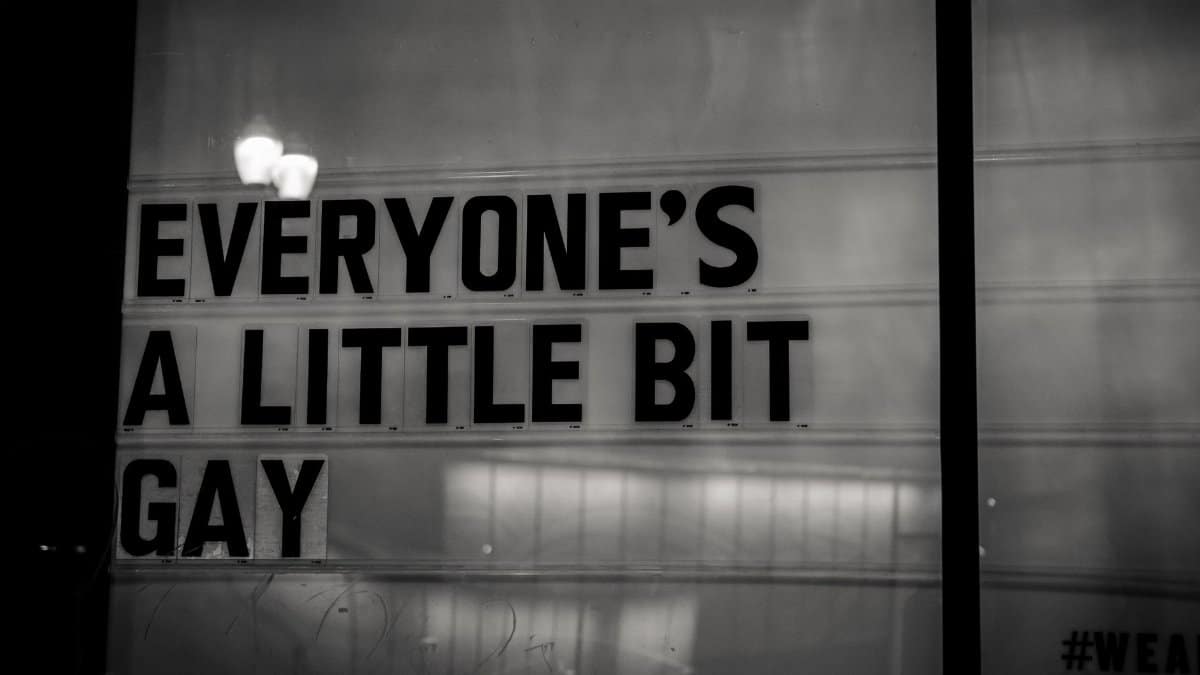 Black and white photo of a sign reading 'Everyone's a little bit gay', promoting inclusivity.