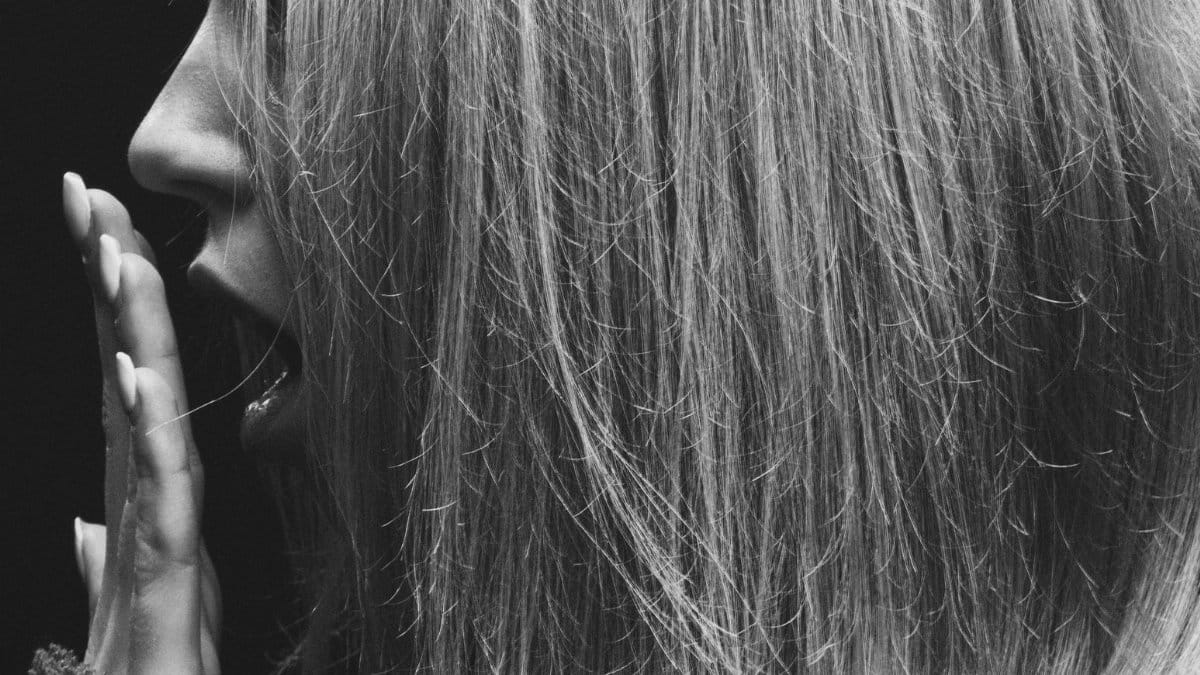 Close-up black and white portrait of a woman yawning, side view, with hand covering mouth. Captured in Kyiv, Ukraine.