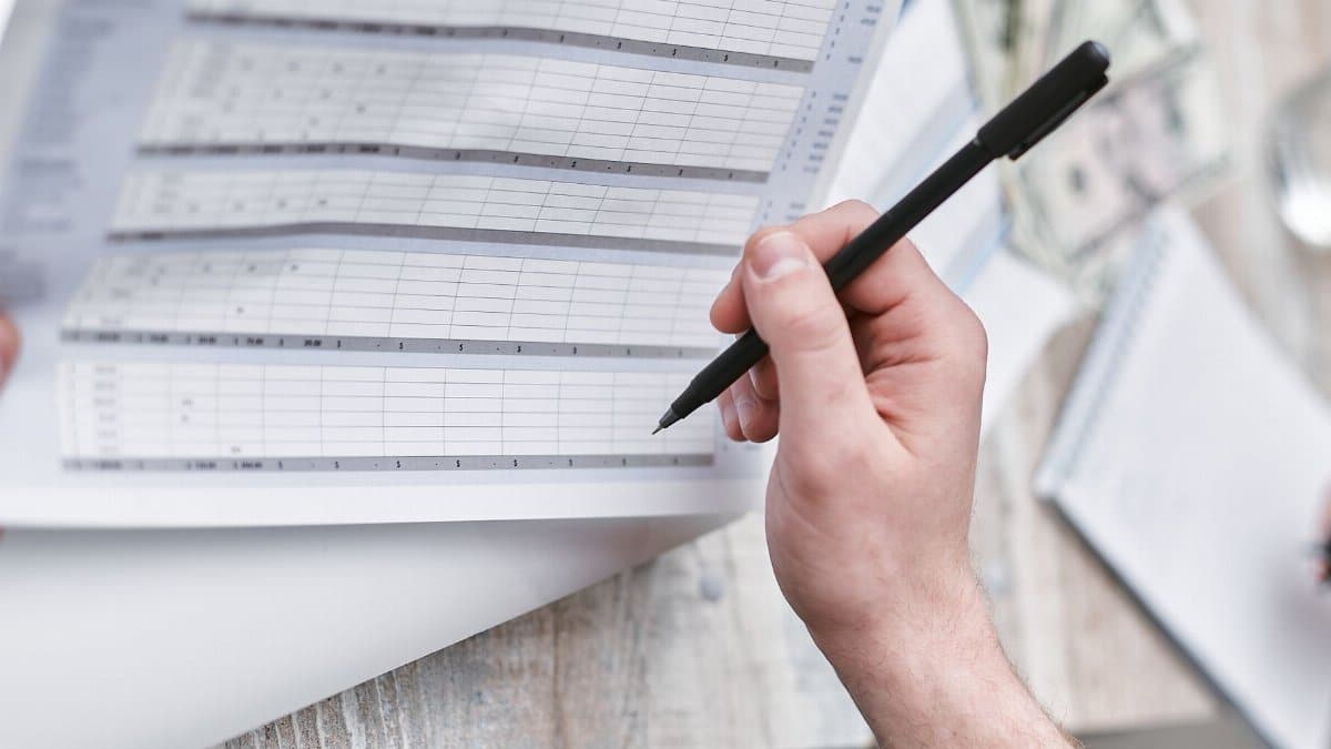 A close-up of a person holding a pen reviewing a financial document with cash visible, ideal for business themes.