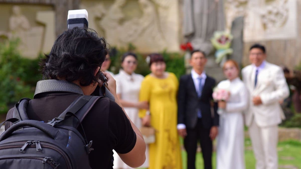 A photographer takes pictures of a wedding ceremony with happy couples and guests outside.
