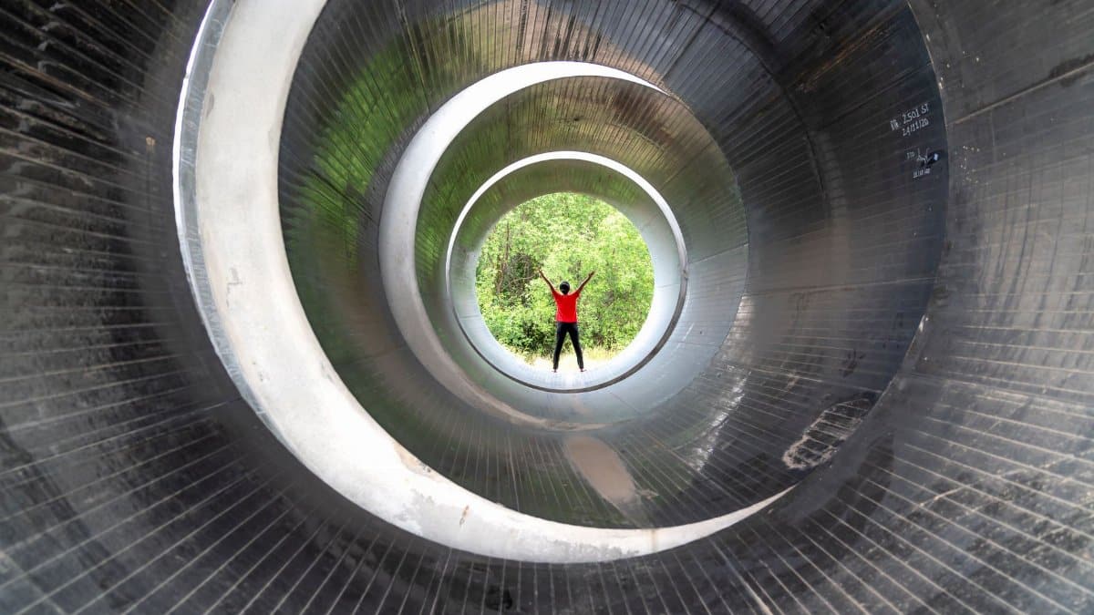 A person stands inside a giant steel tube outdoors, framed by circular openings.