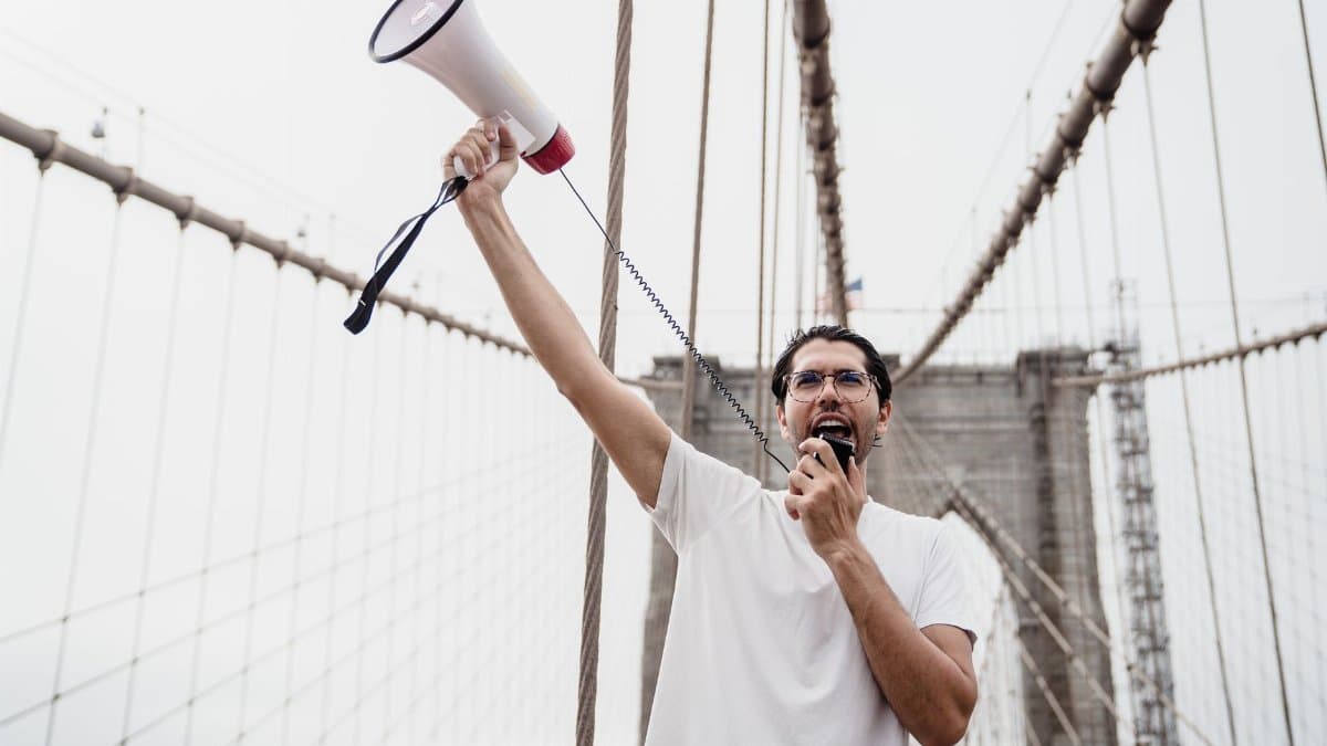 A protester holding a megaphone stands on a famous bridge, voicing support for a cause.