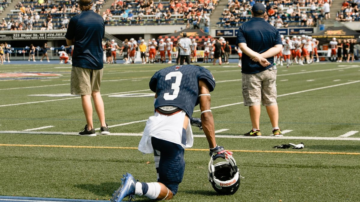 American football player kneels on field during a game in Toronto, Ontario.