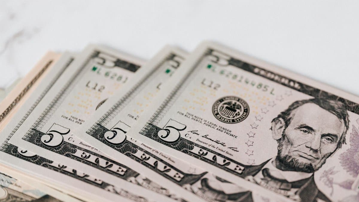 From above of pile of five dollar bills placed on white marble surface