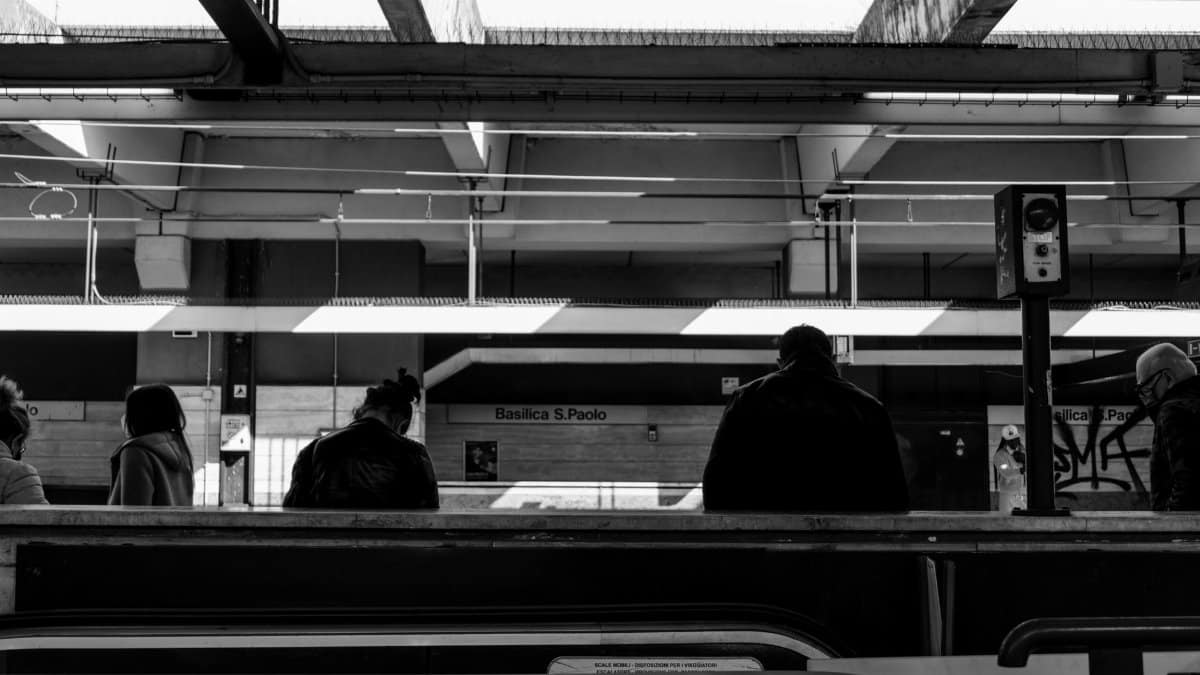 Black and white back view of people standing on station of subway and waiting for train to arrive