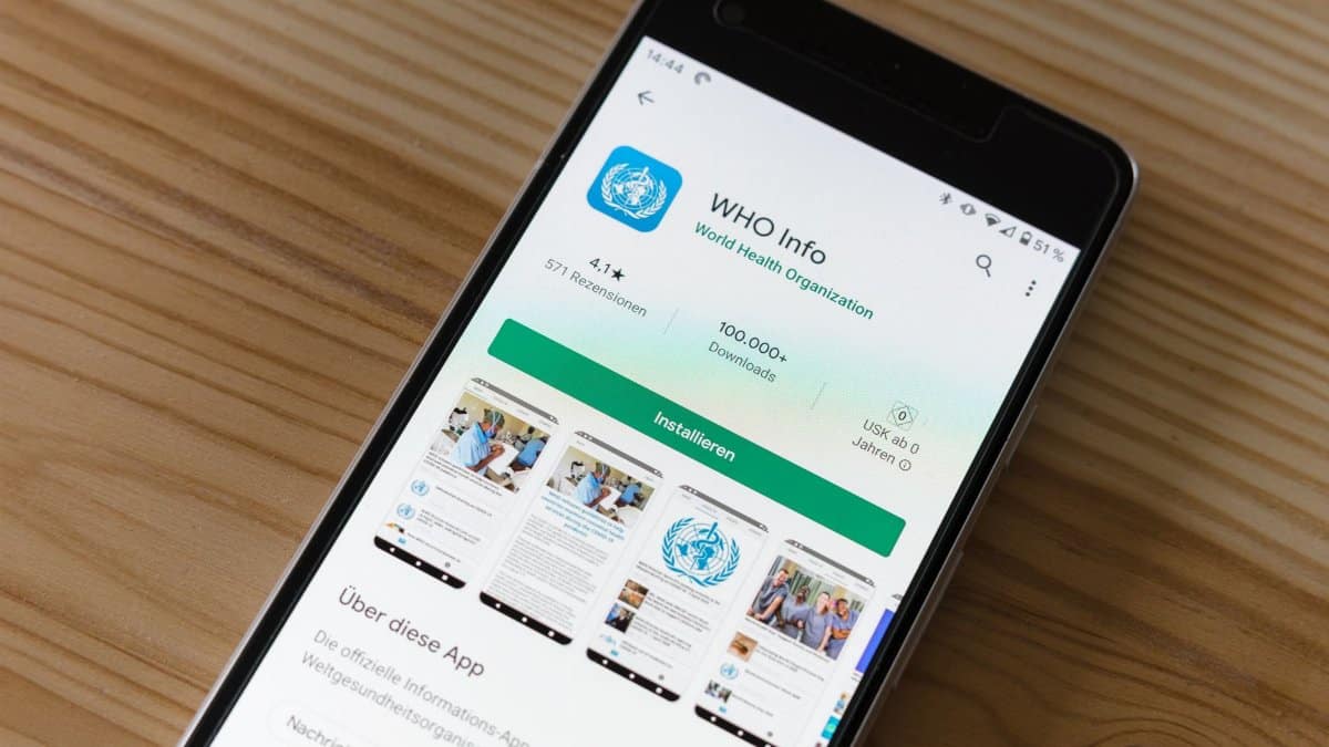 Mobile phone on wooden table showing installation screen for WHO Info app from World Health Organization.