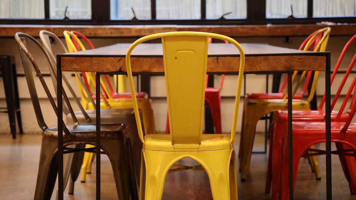 Retro industrial chairs in vibrant colors around a wooden table, indoor loft setting.