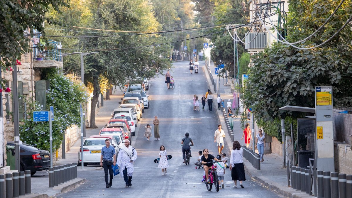 Busy street scene in Jerusalem with people walking and biking on a sunny day.