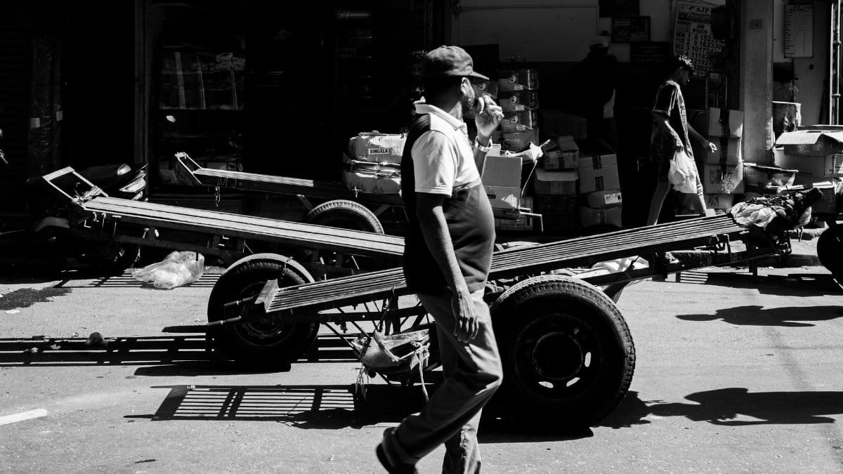 Black and white street scene in Colombo featuring a vendor walking past carts in a bustling market.