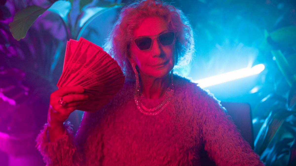 An elderly woman exudes confidence and style under neon lights, holding a fan of cash.
