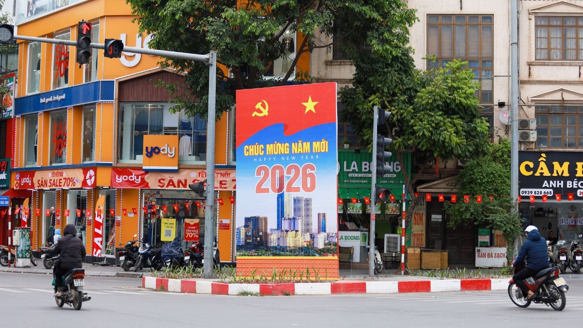 Vibrant Hà Nội street scene featuring a New Year 2026 billboard, motorcycles, and colorful shops.