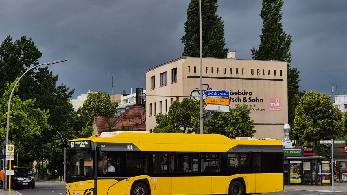Yellow city bus crossing intersection in Berlin with stormy sky and travel agency background.