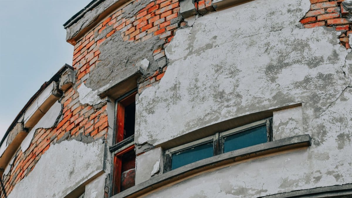 Close-up of a weathered brick building facade showing cracks and deterioration.