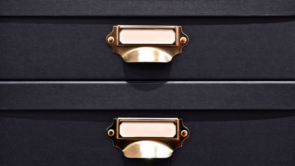 Close-up of black storage boxes featuring elegant brass handles and label holders.