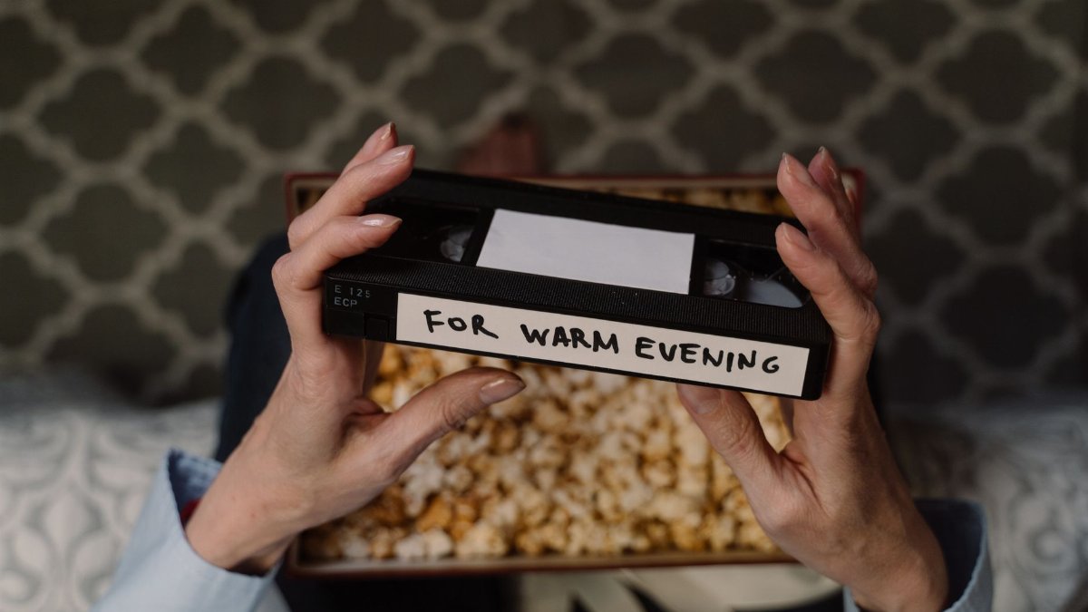 Hands holding a vintage VHS tape labeled 'For Warm Evening' with popcorn in the background.