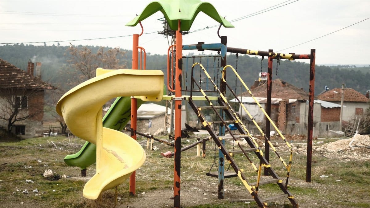 An old, abandoned playground slide and climbing structure in a rural area.