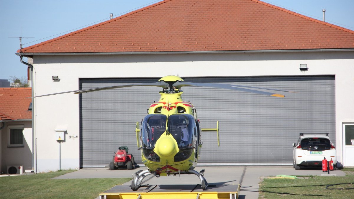 Yellow rescue helicopter on a helipad in front of a hangar, ready for emergency service.