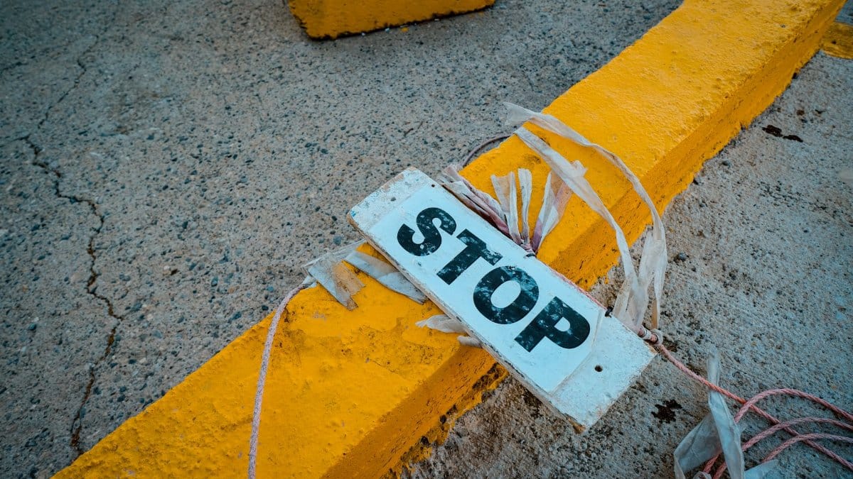 A worn 'STOP' sign placed on a cracked concrete pavement next to a yellow curb.