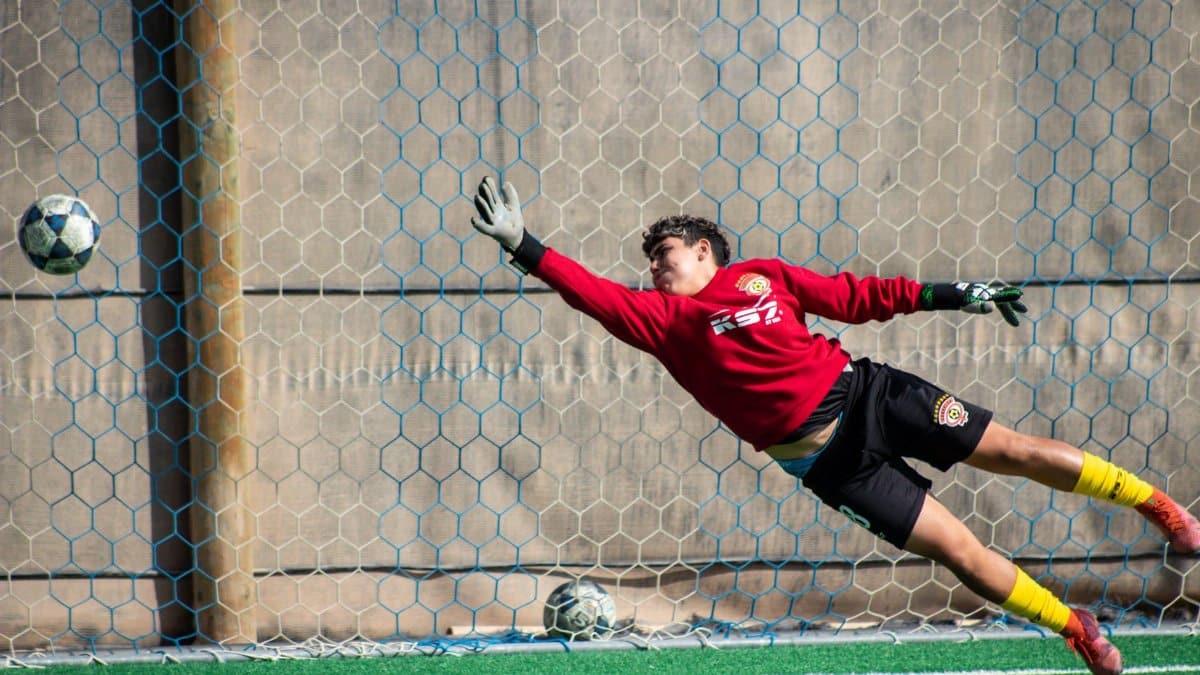 A dynamic shot of a soccer goalkeeper diving to save a ball at a local field in Chile.