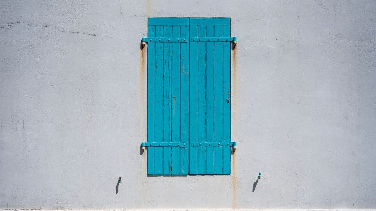 Simple and minimalist exterior shot of closed blue wooden shutters on a white wall.