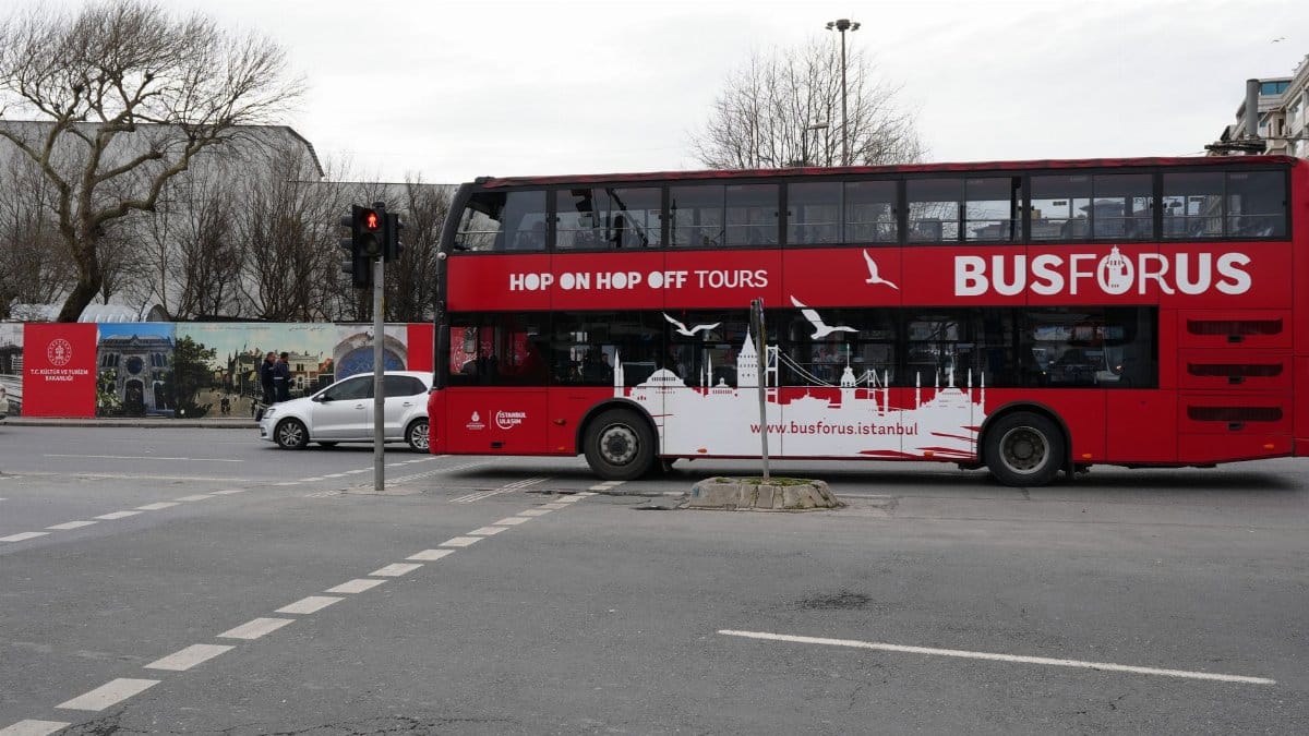 A red double-decker tour bus in İstanbul, featuring iconic city landmarks on its side.