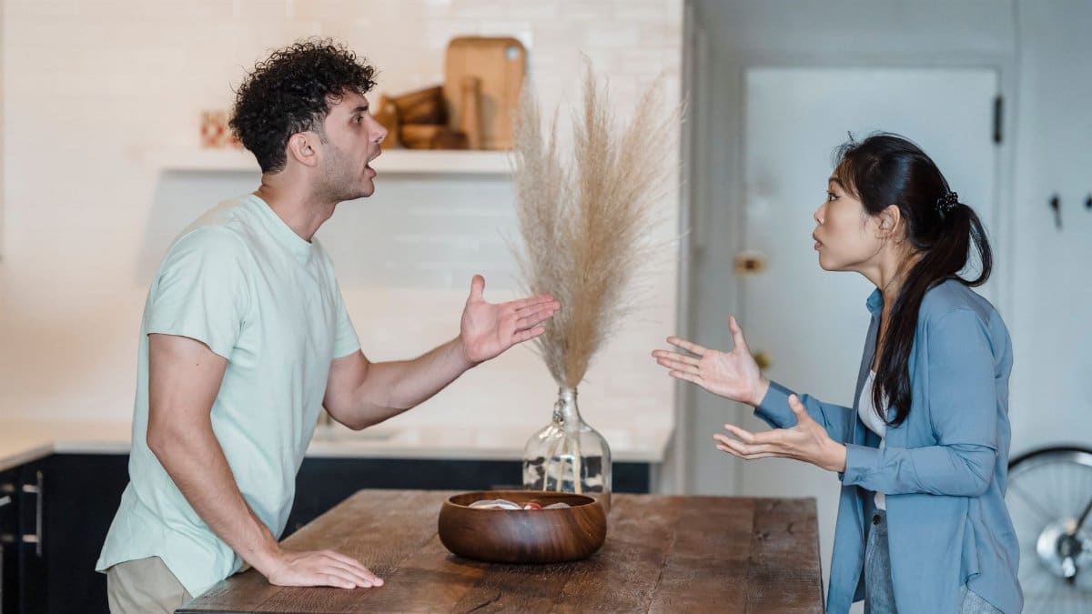 A couple engages in a heated argument at a wooden table in a modern indoor setting.