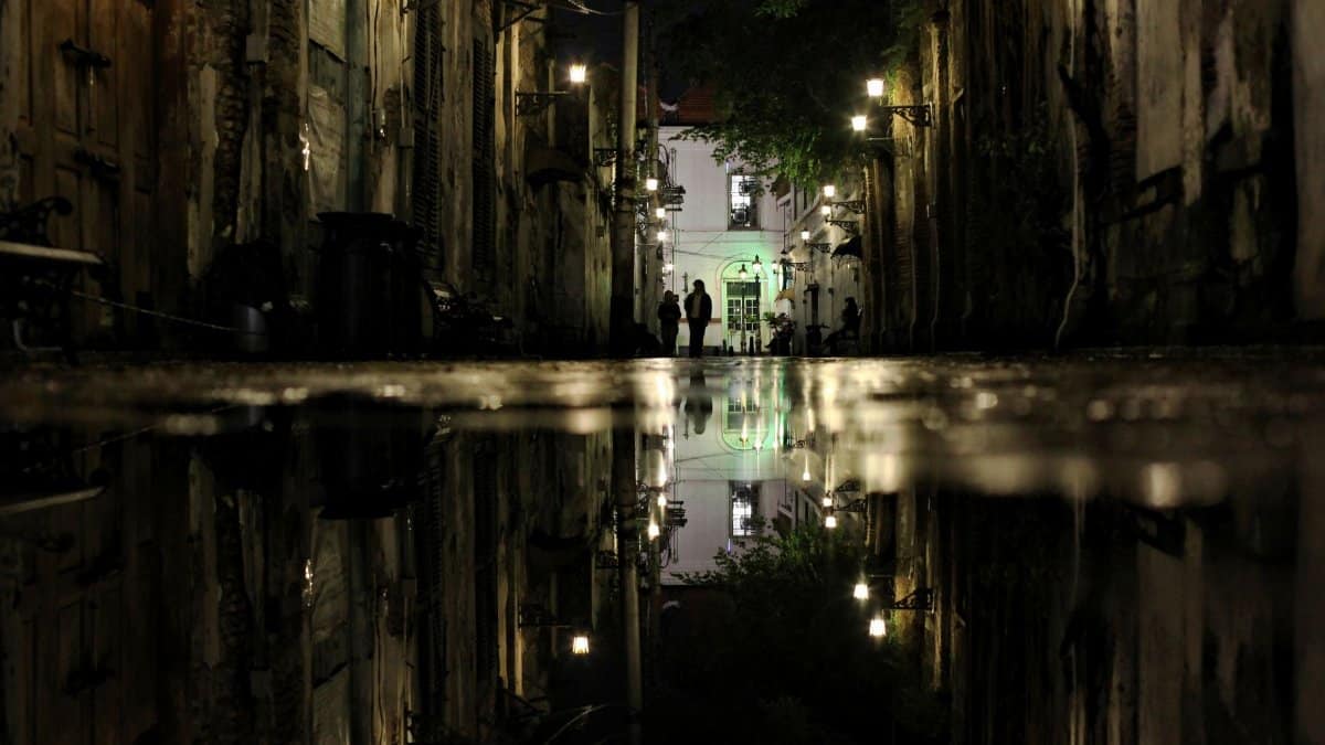 Moody night scene of an alleyway in Semarang with water reflections and street lamps.