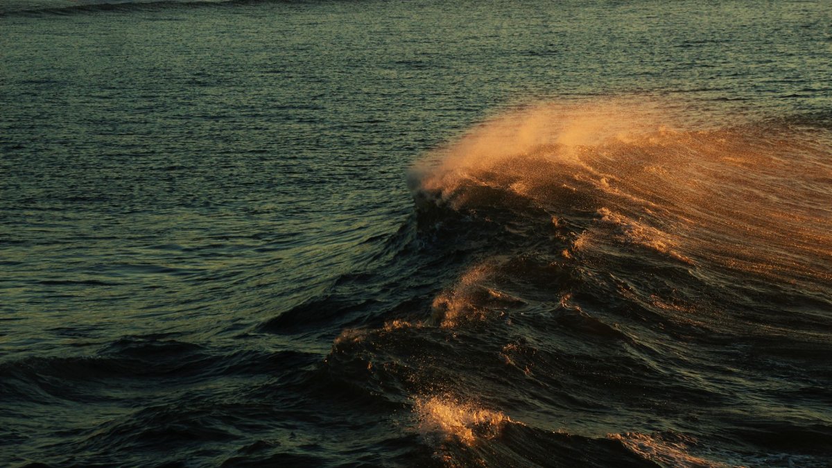 Dynamic ocean waves illuminated by golden sunrise light, creating a dramatic seascape scene.