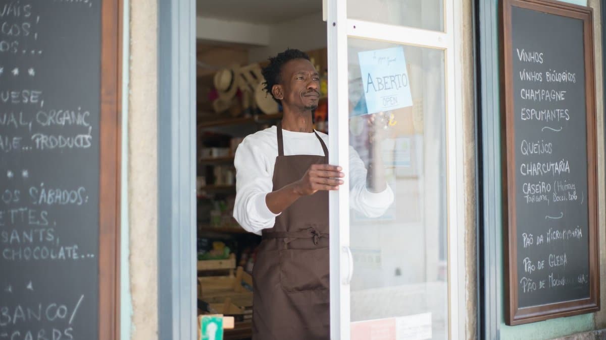 A man in an apron opens a grocery store door in Portugal, ready for business.