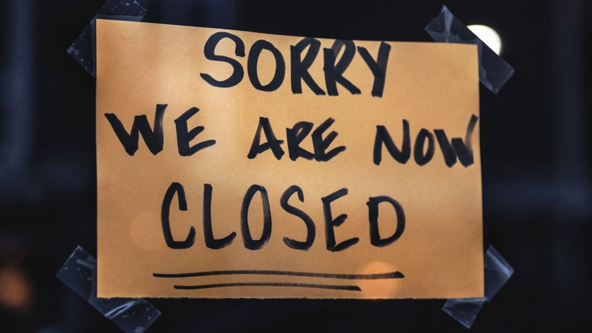 A handwritten sign with 'Sorry We Are Now Closed' in a dark window setting.