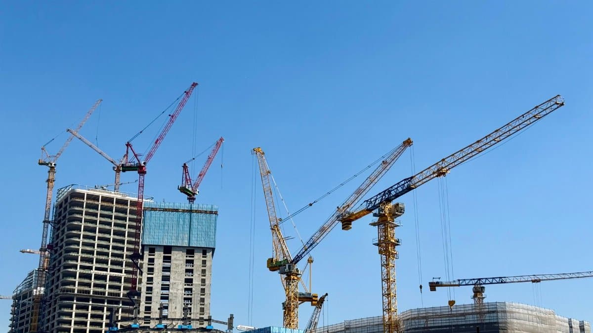 Tower cranes at a skyscraper construction site under a clear blue sky.