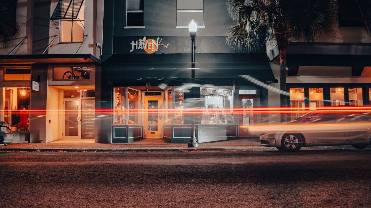 A vibrant street scene at night showcasing motion blur light trails in front of a storefront.
