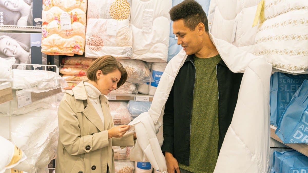 A man and woman selecting bedding in a home goods store, browsing quilt options.