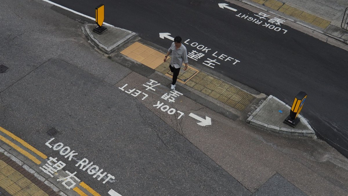 A man walks through a crosswalk in Hong Kong with 'look left' and 'look right' markings.