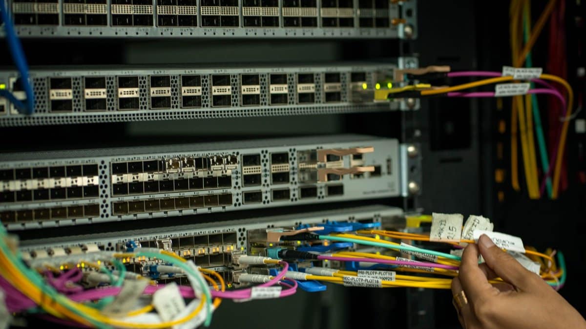 A hand managing fiber optic cables in a server room, showcasing modern connectivity.