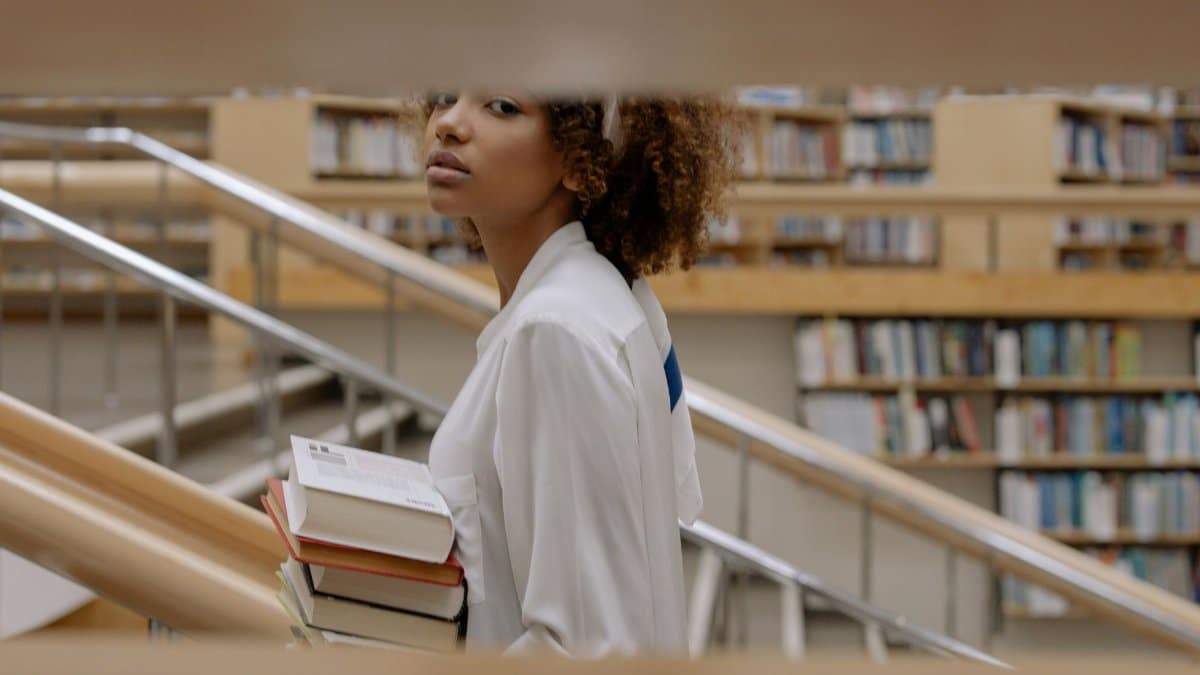Side profile of a woman carrying books in a modern library with blurred shelves.