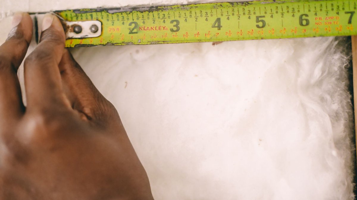 Close-up of a hand measuring insulation with a yellow tape measure.