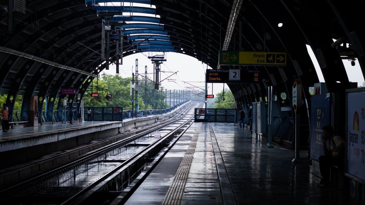 A quiet afternoon at a New Delhi metro station with wet tracks post rain, reflecting urban life.