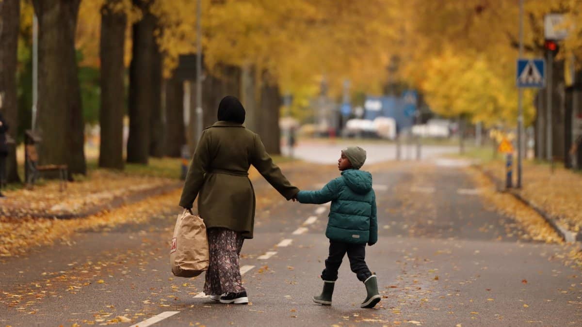 A mother and child holding hands during an autumn walk in Jönköping, Sweden, surrounded by golden leaves on a quiet street.