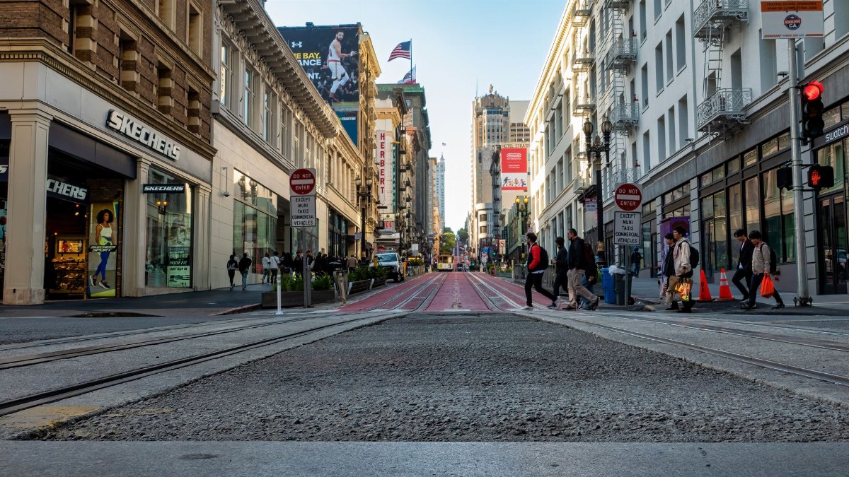 A lively street in San Francisco with people crossing near iconic buildings and shops.