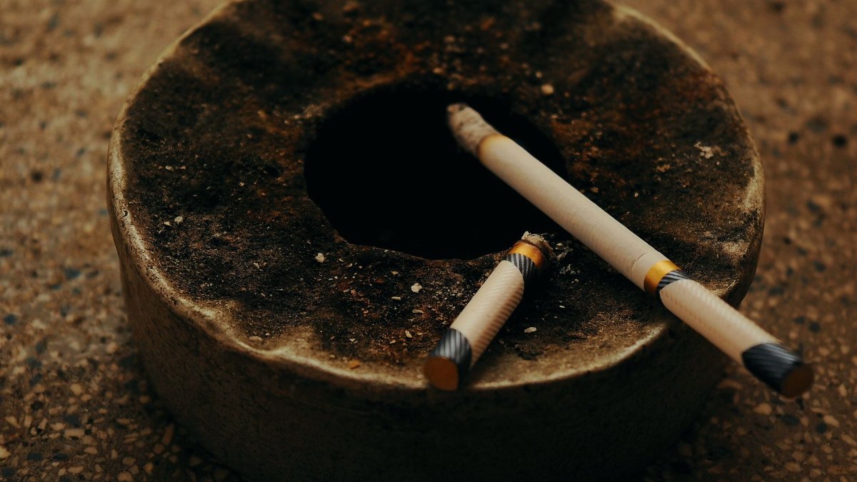 An antique ashtray with two burnt cigarettes on a textured surface, creating a moody atmosphere.